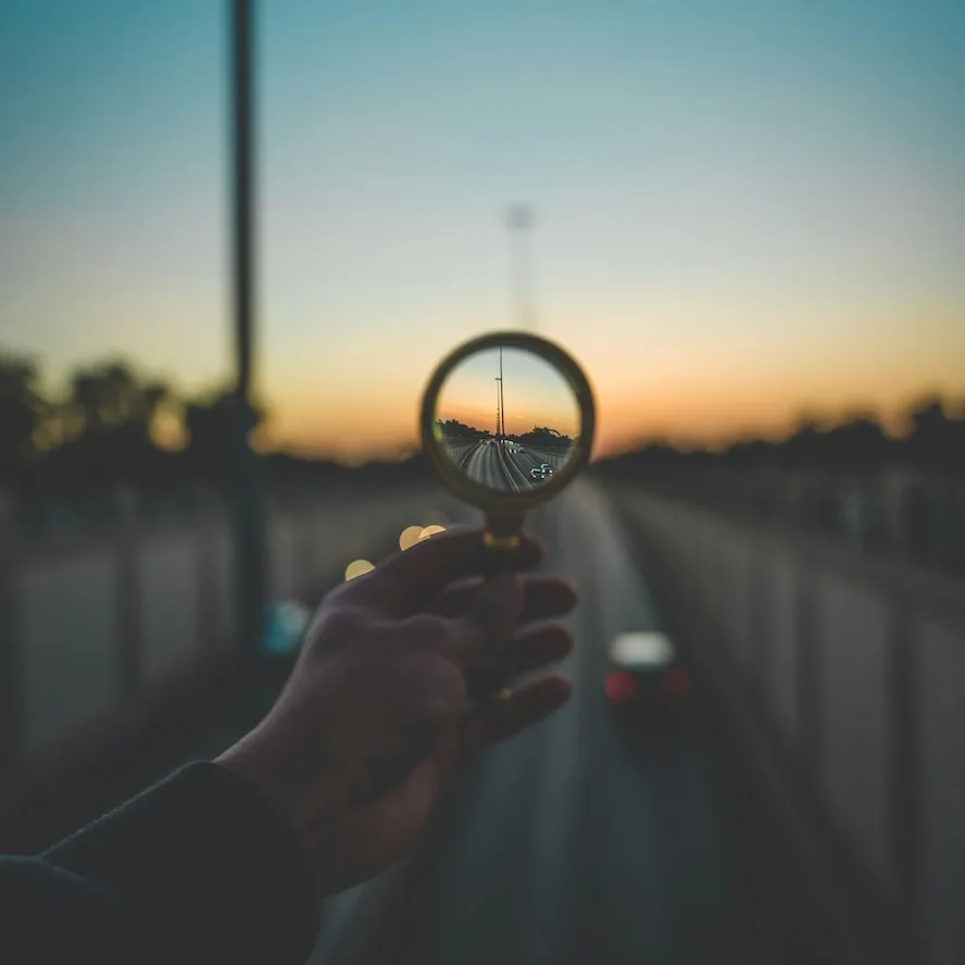 A hand holding a magnifying glass, focusing on a city